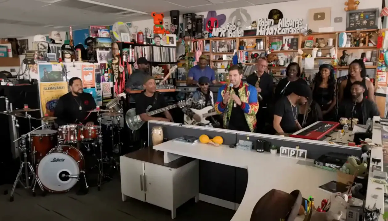Opening wide shot of our actual video, full band behind the desk with the new lead at the center