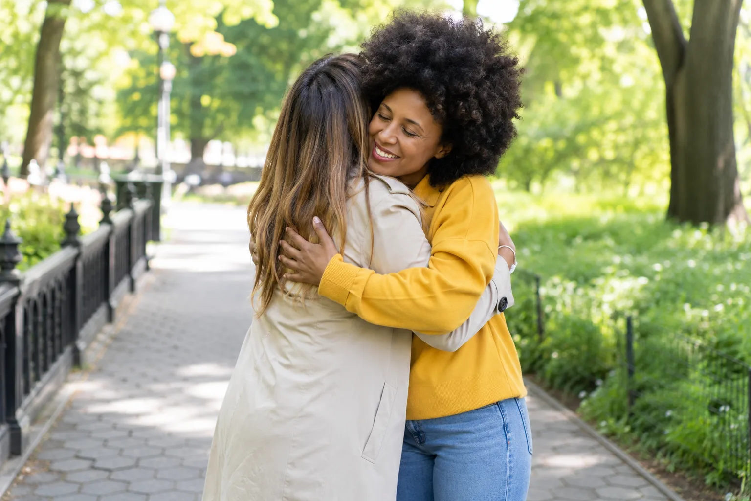 Two fully clothed adult friends sharing a brief, respectful hug in a bright public park, natural candid photography, no children, no text, no logo, no watermark